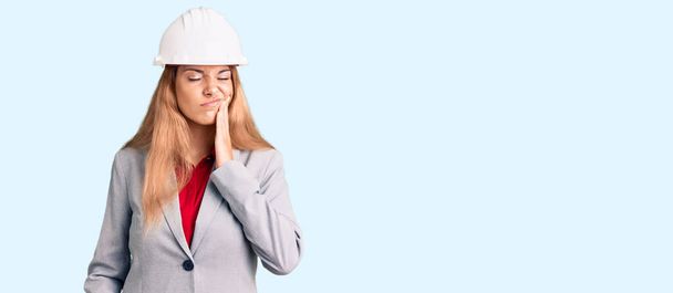 Beautiful young woman wearing architect hardhat touching mouth with hand with painful expression because of toothache or dental illness on teeth. dentist  - Foto, afbeelding