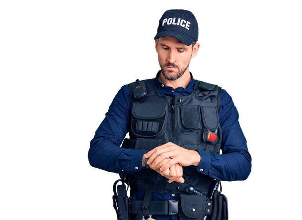 Junger gutaussehender Mann in Polizeiuniform, der an der Armbanduhr die Uhrzeit kontrolliert, entspannt und selbstbewusst  - Foto, Bild