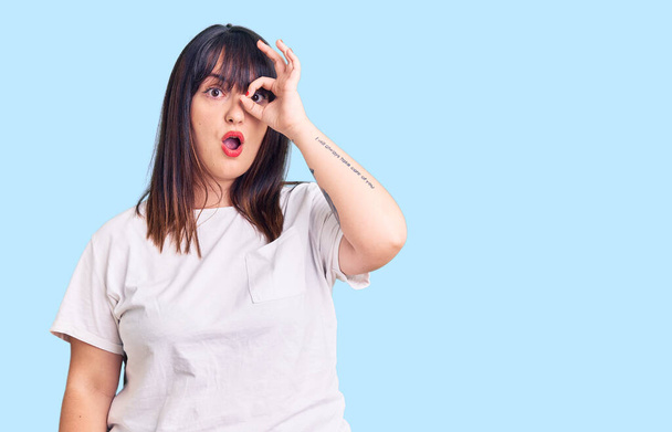 Young plus size woman wearing casual clothes doing ok gesture shocked with surprised face, eye looking through fingers. unbelieving expression.  - Photo, Image