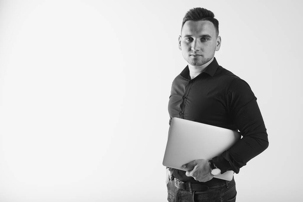 retrato preto e branco de um jovem empresário focado, em uma camisa preta, segurando um laptop, isolado em um fundo branco, há espaço para texto
 - Foto, Imagem