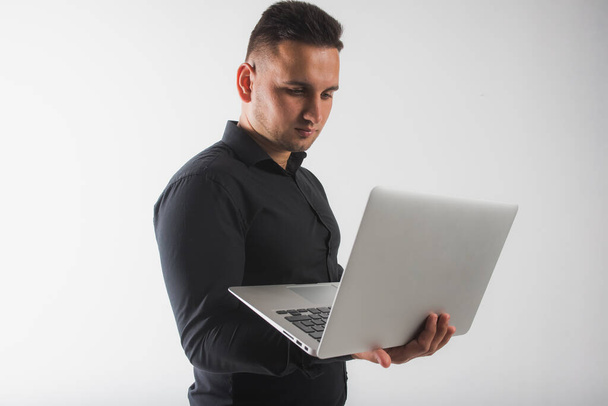 Портрет молодого сфокусированного бизнесмена в костюме, работающего на ноутбуке, стоящего изолированно на белом фоне, есть место для надписи - Фото, изображение