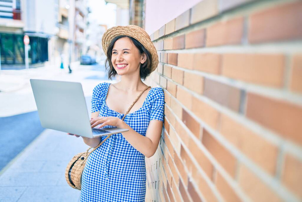 Молода красива дівчина посміхається щаслива, використовуючи ноутбук, що спирається на стіну на вулиці міста
 - Фото, зображення