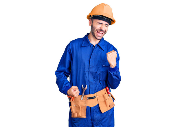 Young hispanic man wearing worker uniform celebrating surprised and amazed for success with arms raised and eyes closed. winner concept.  - Foto, Imagem