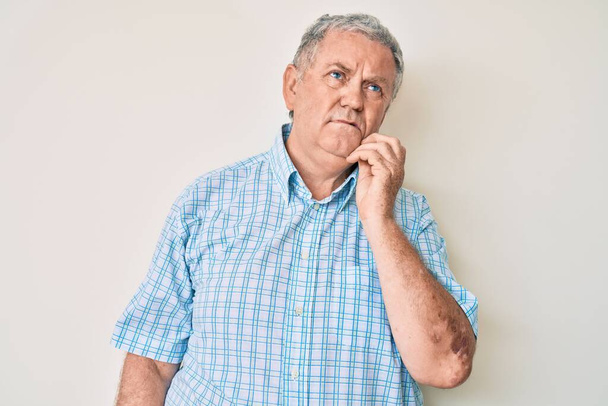 Homme âgé aux cheveux gris portant des vêtements décontractés visage sérieux réfléchissant à la question avec la main sur le menton, réfléchissant à l'idée déroutante  - Photo, image