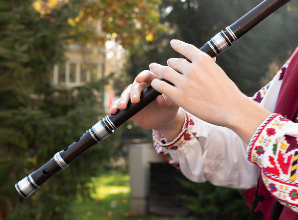 Руки молодого музиканта грають на дерев'яній флейті. Людина в болгарському національному костюмі грає на довгій трубі. Каваль - балканський народний музичний інструмент.. - Фото, зображення