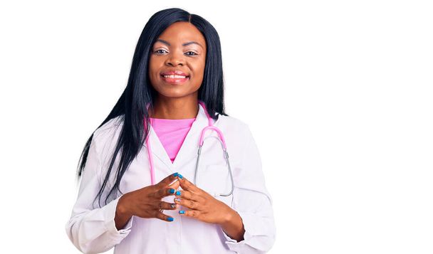Doktor steteskop takan genç Afrikalı Amerikalı kadın ellerini birleştirip gülümseyerek gevşemiş ve neşeyle gülümsüyor. Başarı ve iyimserlik  - Fotoğraf, Görsel