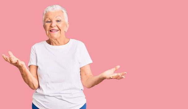 Senior beautiful woman with blue eyes and grey hair wearing casual white tshirt smiling cheerful with open arms as friendly welcome, positive and confident greetings  - 写真・画像