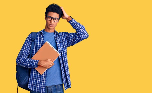 Young african american man wearing student backpack holding book confuse and wondering about question. uncertain with doubt, thinking with hand on head. pensive concept.  - Foto, Bild