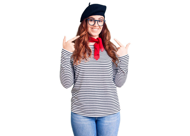 Young beautiful woman wearing french look with beret looking confident with smile on face, pointing oneself with fingers proud and happy.  - Photo, Image