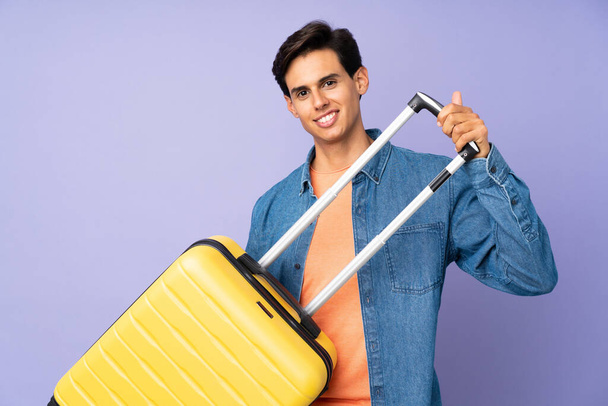 Man over isolated purple background in vacation with travel suitcase - Zdjęcie, obraz