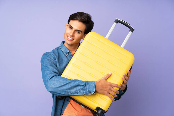 Man over isolated purple background in vacation with travel suitcase - Fotografie, Obrázek