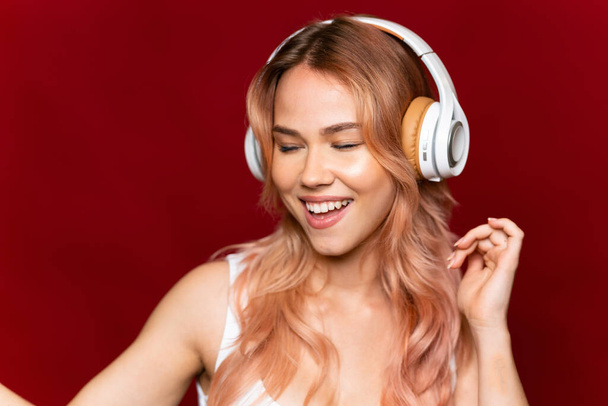 Teini tyttö vaaleanpunaiset hiukset yli eristetty punainen tausta kuuntelee musiikkia ja tanssia - Valokuva, kuva