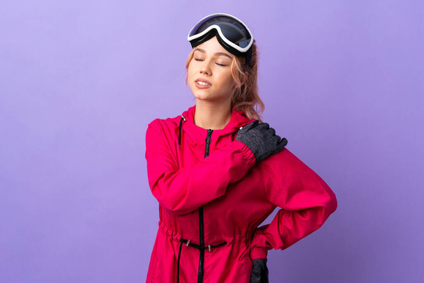 Skier adolescente avec des lunettes de snowboard sur fond violet isolé souffrant de douleur à l'épaule pour avoir fait un effort - Photo, image