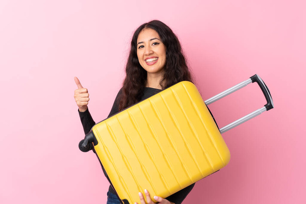 Mixed race woman over isolated pink background in vacation with travel suitcase and with thumb up - Foto, Bild