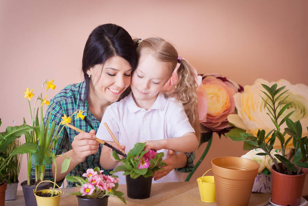 Cute dziewczynka pomaga jej matka do opieki nad roślinami. Szczęśliwa rodzina w studio. - Zdjęcie, obraz