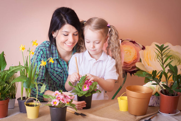 Cute dziewczynka pomaga jej matka do opieki nad roślinami. Szczęśliwa rodzina w studio. - Zdjęcie, obraz