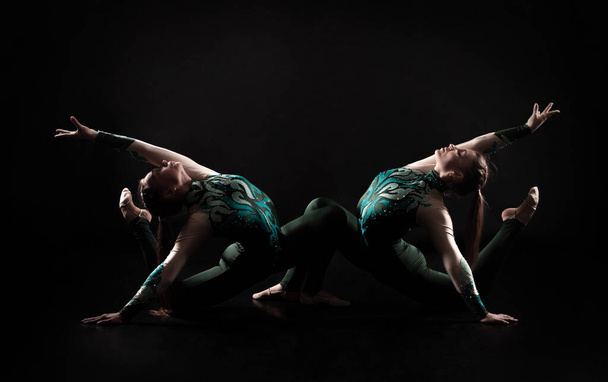 Two young female equilibrists perform acrobatic elements on a dark background in contoured lighting. Studio shooting. - Fotografie, Obrázek