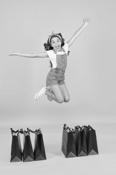 happy jump. online shopping for kids. give-away concept. ready for holiday celebration. little girl after successful shopping. happy childhood. child with package bags. buy presents on cyber monday - Photo, Image