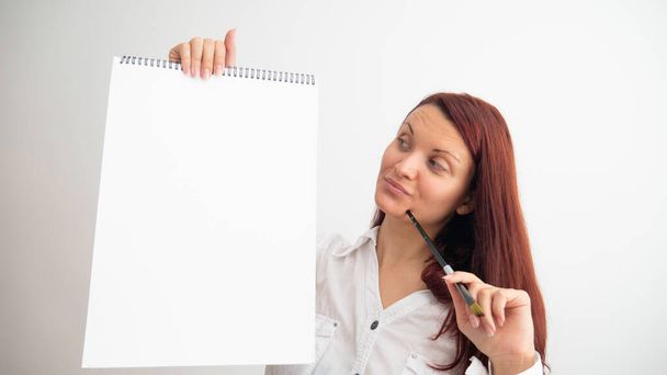 Beautiful woman posing, holding a paintbrush, artist in white t-shirt. White blank canvas pad. - Fotó, kép