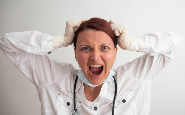 A female doctor or nurse screams into the camera. Doctor in white medical coat mad shouting and yelling with aggressive expression. Frustration concept, isolated white background. - Photo, Image