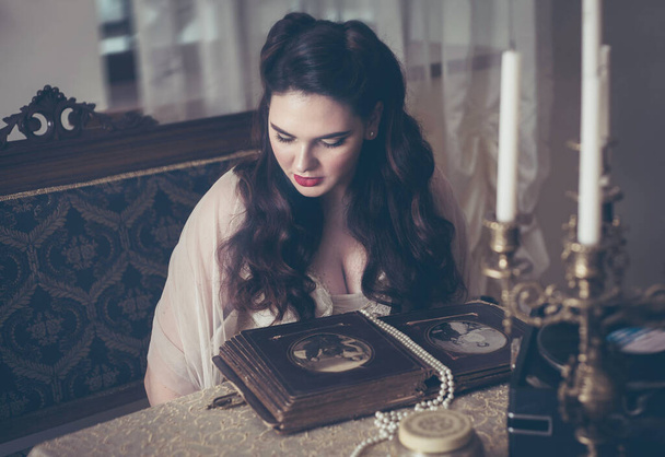 Une jeune femme regarde un album photo. Ancien style vintage, intérieur rétro. - Photo, image