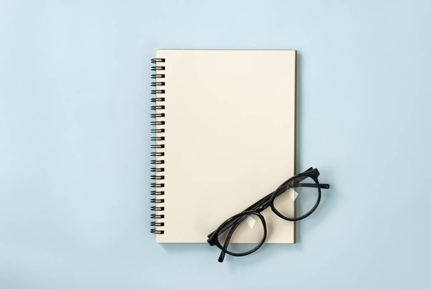 Cuaderno en espiral o cuaderno de primavera en tipo sin forro y gafas graduadas sobre fondo minimalista de pastel azul. Cuaderno espiral Mockup en el marco del centro - Foto, imagen