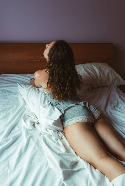 Νεαρή γυναίκα στο πιτζάμα ξαπλωμένη μπρούμυτα στο κρεβάτι. Μη αναγνωρίσιμο  - Φωτογραφία, εικόνα