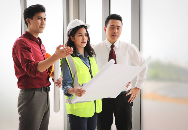 Group of three construction workers, one woman and two men standing by windows , holding blue print and  discussing about  project. - Photo, Image