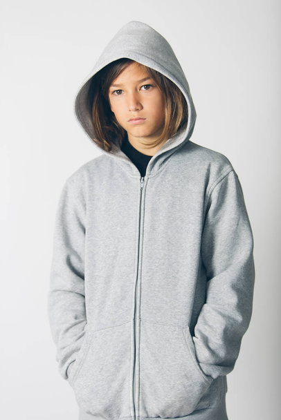 Eleven years old boy with hooded sweater standing against a white background - Фото, изображение