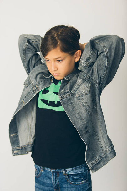 Eleven years old boy with a jean jacket standing against a white background - Photo, image