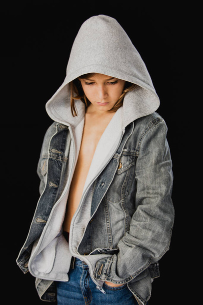 Jedenáct let starý chlapec s kapucí svetr a džínová bunda stojí na černém pozadí - Fotografie, Obrázek