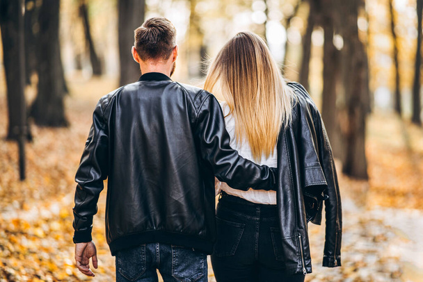 Portret zakochanej pary spacerującej na świeżym powietrzu w jesiennym parku. Mężczyzna i kobieta trzymający się za ręce. Widok z tyłu. - Zdjęcie, obraz