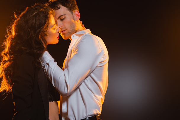 man in shirt touching curly girlfriend in blazer on black  - Φωτογραφία, εικόνα