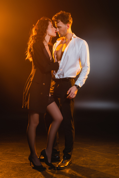 seductive woman in blazer and stockings touching sexy boyfriend in suit on black  - 写真・画像
