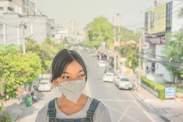 Koncept zdravotní péče. Mladá dívka v masce obličeje na ulici města, asijská dívka nosí masku ochrany dýchacích cest N95 proti znečištění ovzduší PM2.5 a bolesti hlavy Udusit. - Fotografie, Obrázek