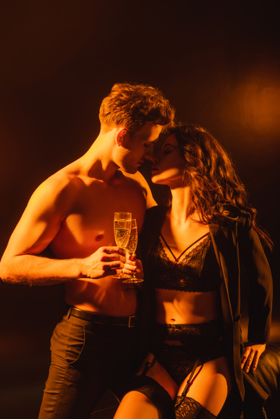 sexy couple with closed eyes holding glasses with champagne while clinking on black  - Fotó, kép
