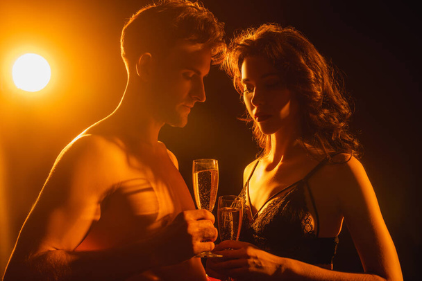 sexy couple holding glasses with champagne on black with back light - Fotografie, Obrázek