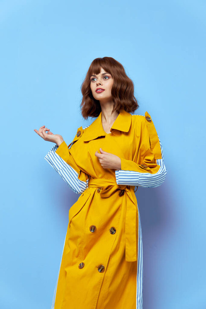  woman in a yellow coat gestures with her hands on a blue background and looks to the side - Photo, image