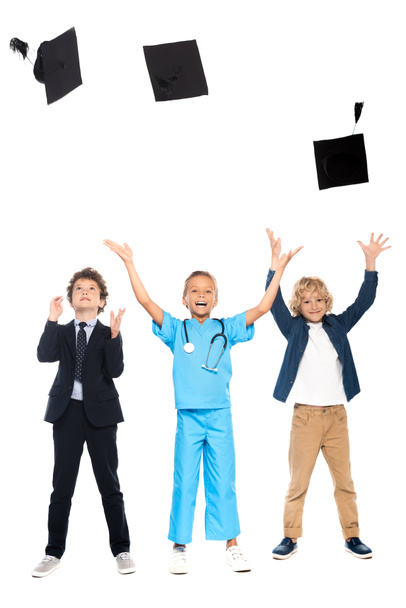 kids dressed in costumes of different professions throwing in air graduation caps isolated on white  - Фото, изображение