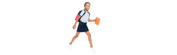 Gözlüklü heyecanlı okul çocuğunun yatay görüntüsü. Beyaz üzerinde yürürken kitap tutuyor.  - Fotoğraf, Görsel