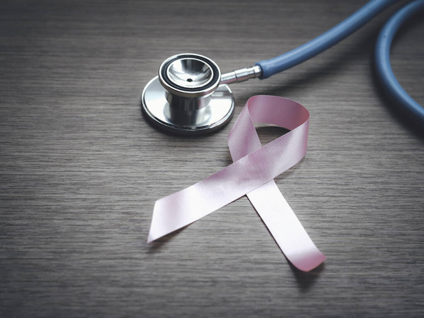 Różowa wstążka świadomości raka piersi ze stetoskopem lekarskim na drewnianym tle, symbol października, koncepcja opieki zdrowotnej i medycyny - Zdjęcie, obraz