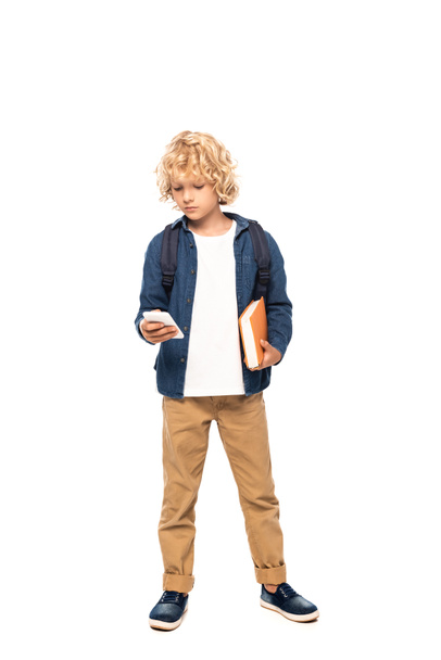 blonde schoolboy holding book and using smartphone isolated on white  - Photo, image