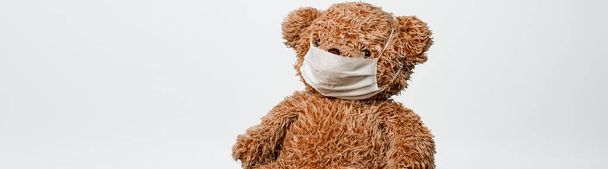 Teddy bear toy is sitting in white medical mask on a white background. Concept of illness, hygiene and virus protection for children - Foto, Bild