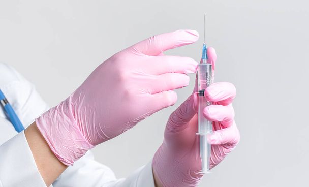 Close-up doctor's hand in pink rubber gloves holding a syringe. Focus at syringe. Vaccination concept. - Photo, Image