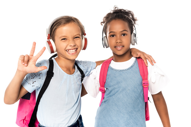 Μαθητής ακούει μουσική σε ασύρματα ακουστικά, αγκαλιάζει Αφροαμερικανό φίλο και δείχνει τρία δάχτυλα απομονωμένα σε λευκό  - Φωτογραφία, εικόνα