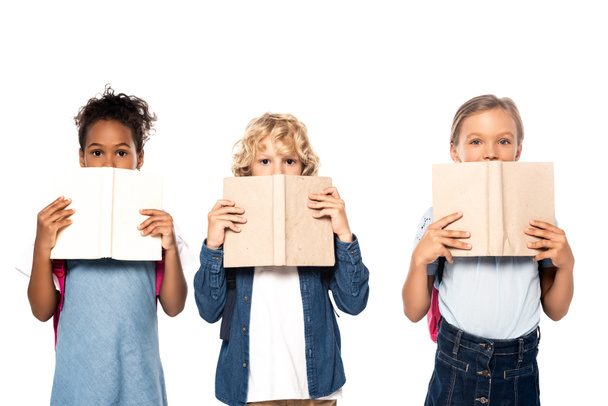 школьниц и школьников, покрывающих лица книгами и смотрящих на камеру, изолированную на белом  - Фото, изображение