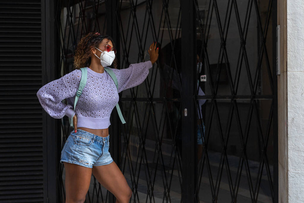 Giovane bella donna nera in attesa di entrare a casa con maschera per strada. - Foto, immagini
