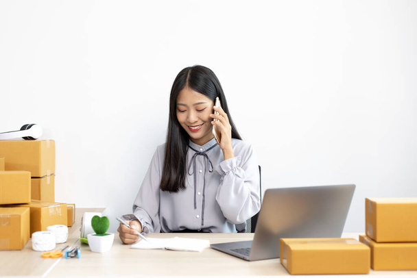 Asian businesswoman is taking online orders from a phone and chatting with customers to confirm their order, Selling products online or doing freelance work at home concept. - Photo, Image
