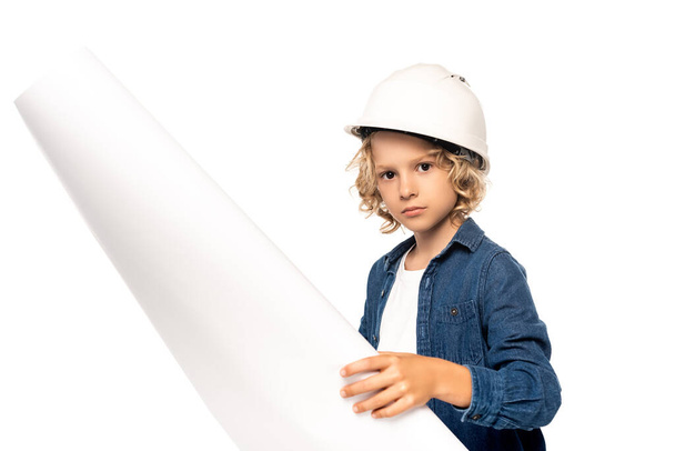 αγόρι σε κράνος ασφαλείας και κοστούμι του αρχιτέκτονα κρατώντας σχέδιο και κοιτάζοντας κάμερα που απομονώνονται σε λευκό - Φωτογραφία, εικόνα