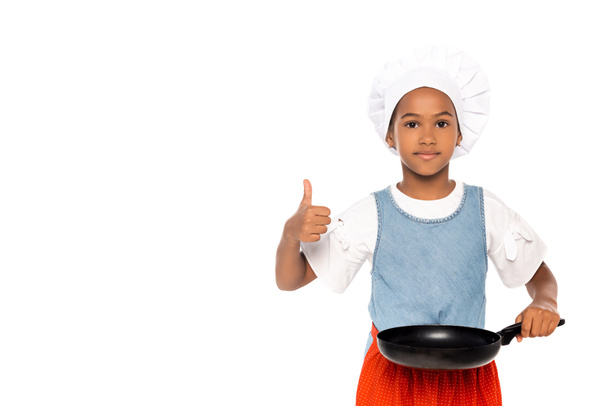 Niño afroamericano disfrazado de chef mostrando el pulgar hacia arriba mientras sostiene la sartén aislada en blanco  - Foto, Imagen